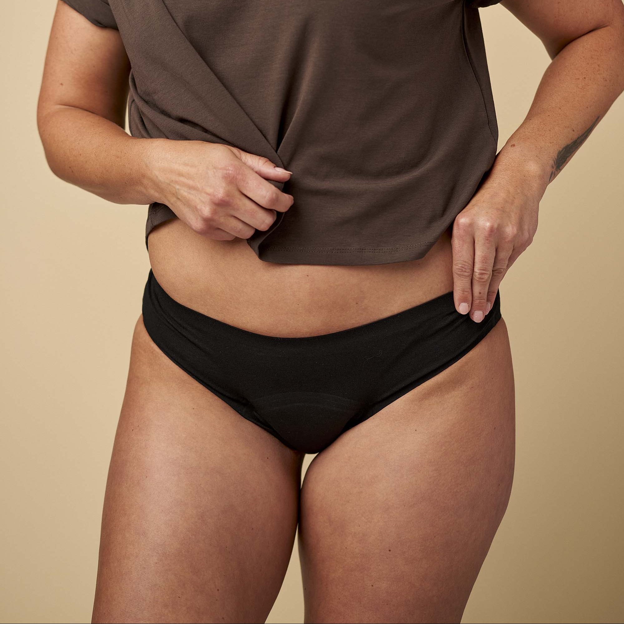 Person wearing a brown t-shirt and black underwear on a beige background