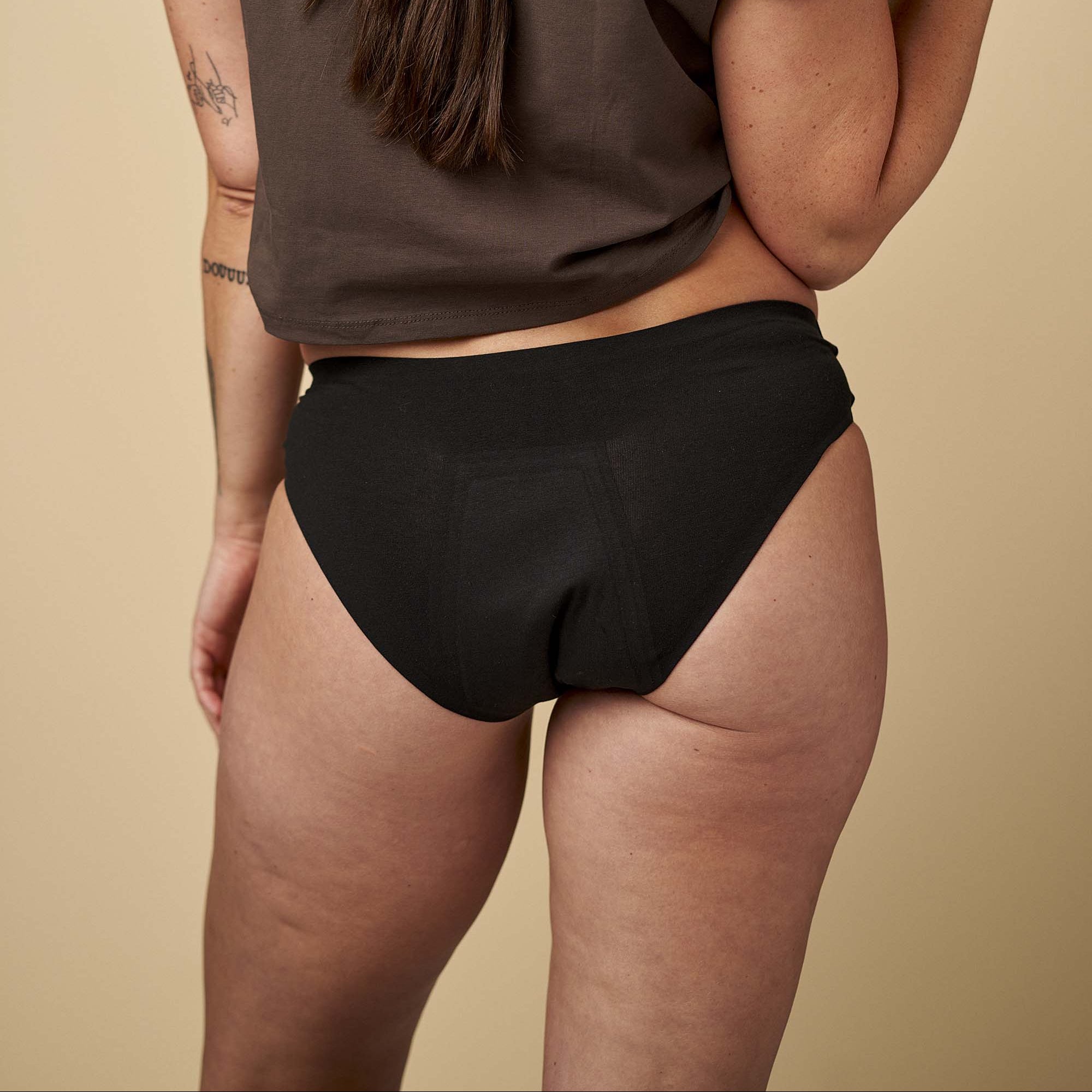 Person wearing a brown t-shirt and black underwear on a beige background